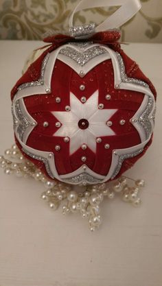 a red and white ornament hanging from a string on a table with pearls