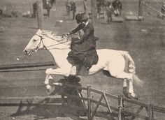 an old black and white photo of a person on a horse jumping over a fence