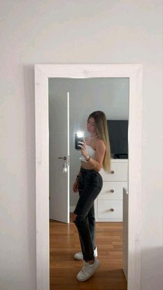 a woman standing in front of a mirror taking a selfie with her cell phone