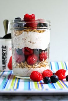 a glass jar filled with yogurt, berries and granola on top of a table