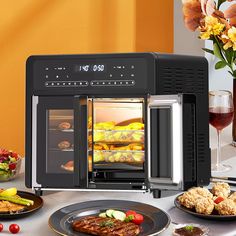 an open oven with food in it on a table next to plates and wine glasses