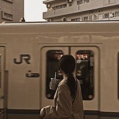 a woman is waiting for the train to arrive at the station with her coffee in hand