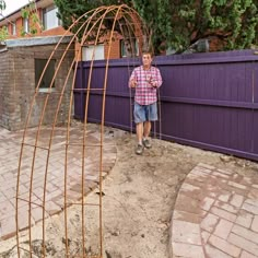 a man standing next to a purple fence with a wooden structure in front of him