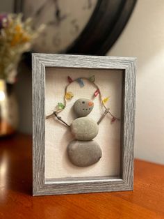 a small white frame with a rock in the shape of a snowman on it