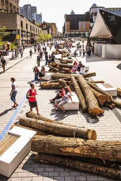 people are sitting on benches made out of logs in the middle of a city square