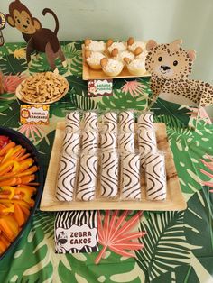 a table topped with lots of food and desserts next to jungle animals on the wall