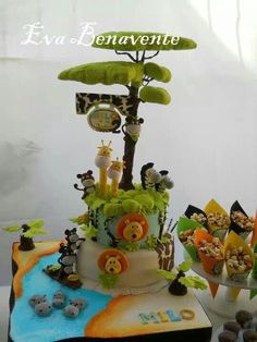 a cake decorated with animals and plants on top of a table next to cupcakes