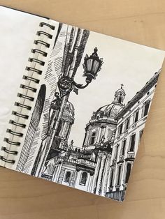 a notebook with a drawing of a street light and buildings in the background on a wooden table