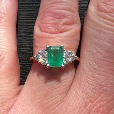 an emerald and diamond ring on someone's finger