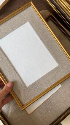 a person is holding up a frame with white paper in it on top of a table