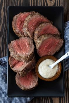 sliced steak on a black plate with ranch dressing in a small bowl next to it