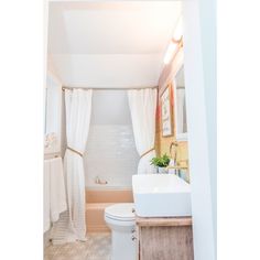 a white toilet sitting next to a bath tub under a bathroom window covered in curtains