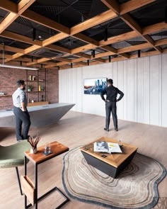 two men standing in an office with exposed ceilings and wooden flooring, looking at artwork on the wall