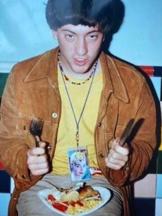 a young man sitting in front of a plate with food on it and holding utensils