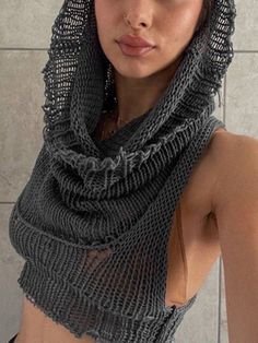 a woman wearing a gray knitted shawl over her head and shoulders, in front of a tiled wall