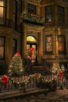 christmas lights decorate the front of an old building with wreaths and garlanded trees