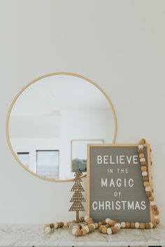 a sign that says believe in the magic of christmas next to a small tree on a mantle