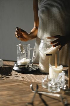 a person pouring sugar into a blender on top of a wooden table next to other items