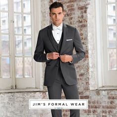 Man standing in the corner of a room in a vacant brick building.  A white window on each side.  Man wearing the Michael Kors Steel Grey Sterling wedding suit from JFW.