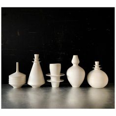 five white vases sitting on top of a table next to each other in front of a black wall