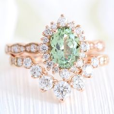 a close up of a ring with an oval shaped green stone surrounded by smaller round diamonds