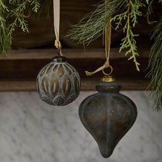 two ornaments hanging from a christmas tree in front of a marble wall and wood ceiling