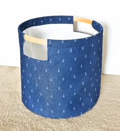 a blue fabric basket with an anchor pattern on the front and sides, sitting on a carpeted floor