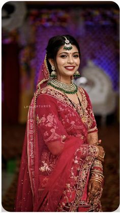 a woman in a red and gold bridal outfit with jewelry on her head, smiling at the camera