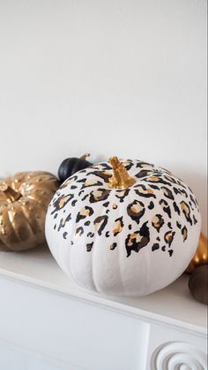 two decorative pumpkins sitting on top of a white mantle with gold decorations around them