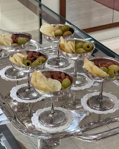 an assortment of olives and chips in wine goblets on a silver tray