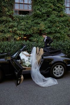 a man in a tuxedo standing next to a black sports car