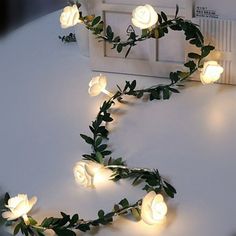 white roses and leaves are arranged on a table with some light up lights in the shape of letters