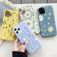 three phone cases with flowers on them are sitting on a table next to a woman's hand