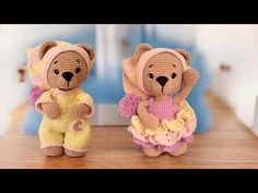 two crocheted teddy bears dressed in pink and yellow outfits sitting on a table