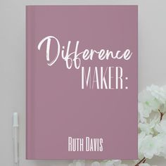 a pink book with the words differences maker written on it next to some white flowers