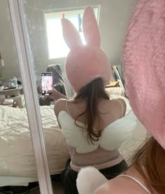 a woman taking a selfie in front of a mirror wearing a pink bunny ears hat