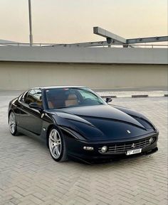 a black sports car parked in front of a building on a brick road next to a bridge