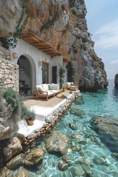 a house sitting on top of a rocky cliff next to the ocean with blue water