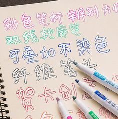 three markers are placed on top of a notebook with chinese characters written in different colors