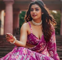 a woman sitting on steps wearing a pink dress and pearls necklaces, with her hands in the air