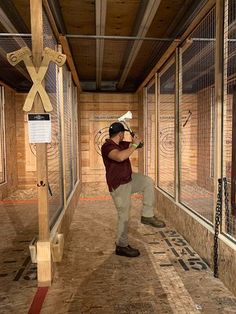 a man holding a baseball bat while standing in front of a caged area filled with animals