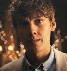 a man in a suit and tie looking at the camera with blurry lights behind him