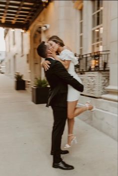 a man and woman are kissing on the sidewalk in front of a building with windows