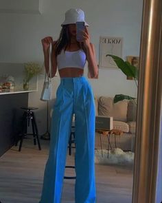 a woman taking a selfie while wearing blue pants and a white cropped top