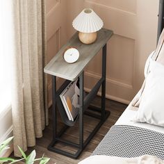 a table with magazines and a lamp on it in front of a window next to a bed