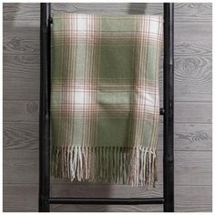 a green and white plaid blanket hanging on a black metal rack against a wooden wall