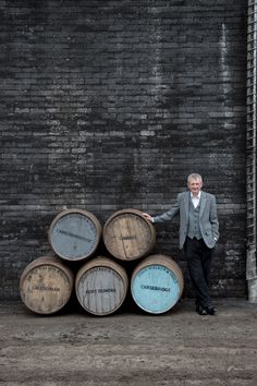 a man standing next to some barrels in front of a brick wall