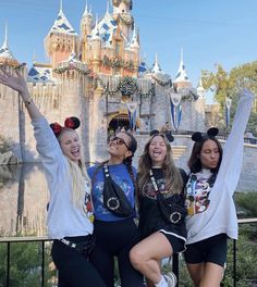 three girls are posing in front of a castle with their arms up and one girl is wearing mickey ears