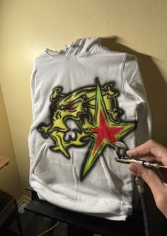 someone is drawing on a white hoodie with red, yellow and green stars in the middle