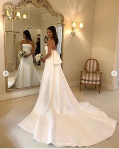 a woman standing in front of a mirror wearing a wedding dress with bow at the waist